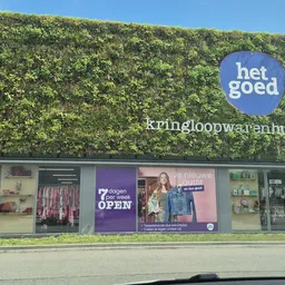Gevel van kringloopwinkel met groene klimopbekleding, ramen met spullen en reclameposters