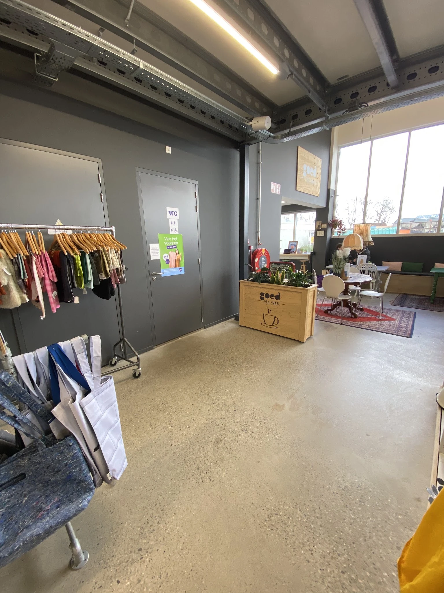 Winkelinterieur met kledingrek, houten plantenbak en winkelruimte met daglicht van buiten
