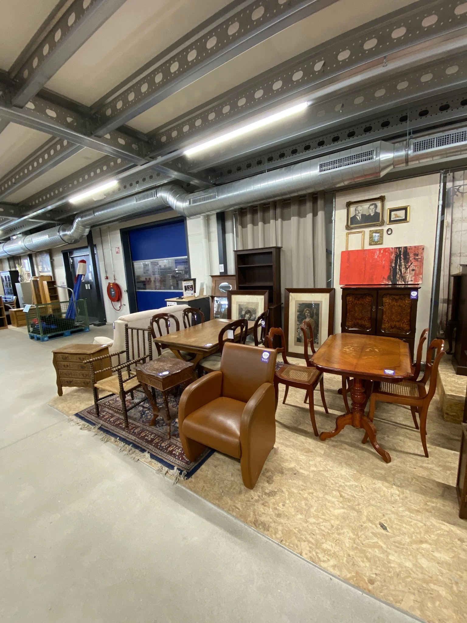 Diverse meubels in een kringloopwinkel, waaronder houten stoelen, tafels, een bruine fauteuil en kasten.