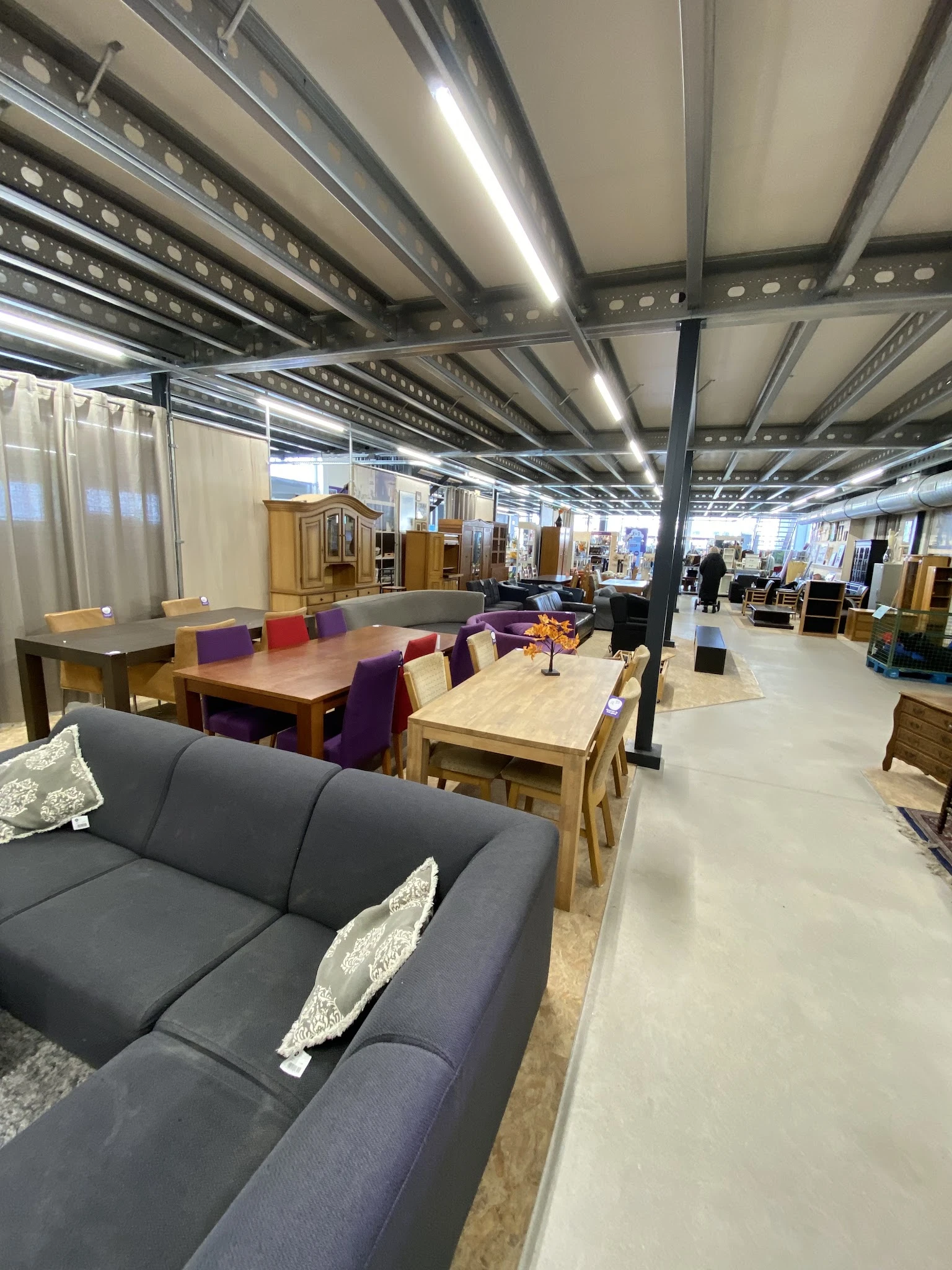 Ruime kringloopwinkel met meubels, tafels, stoelen en kasten uitgestald op een heldere vloer onder industriële verlichting