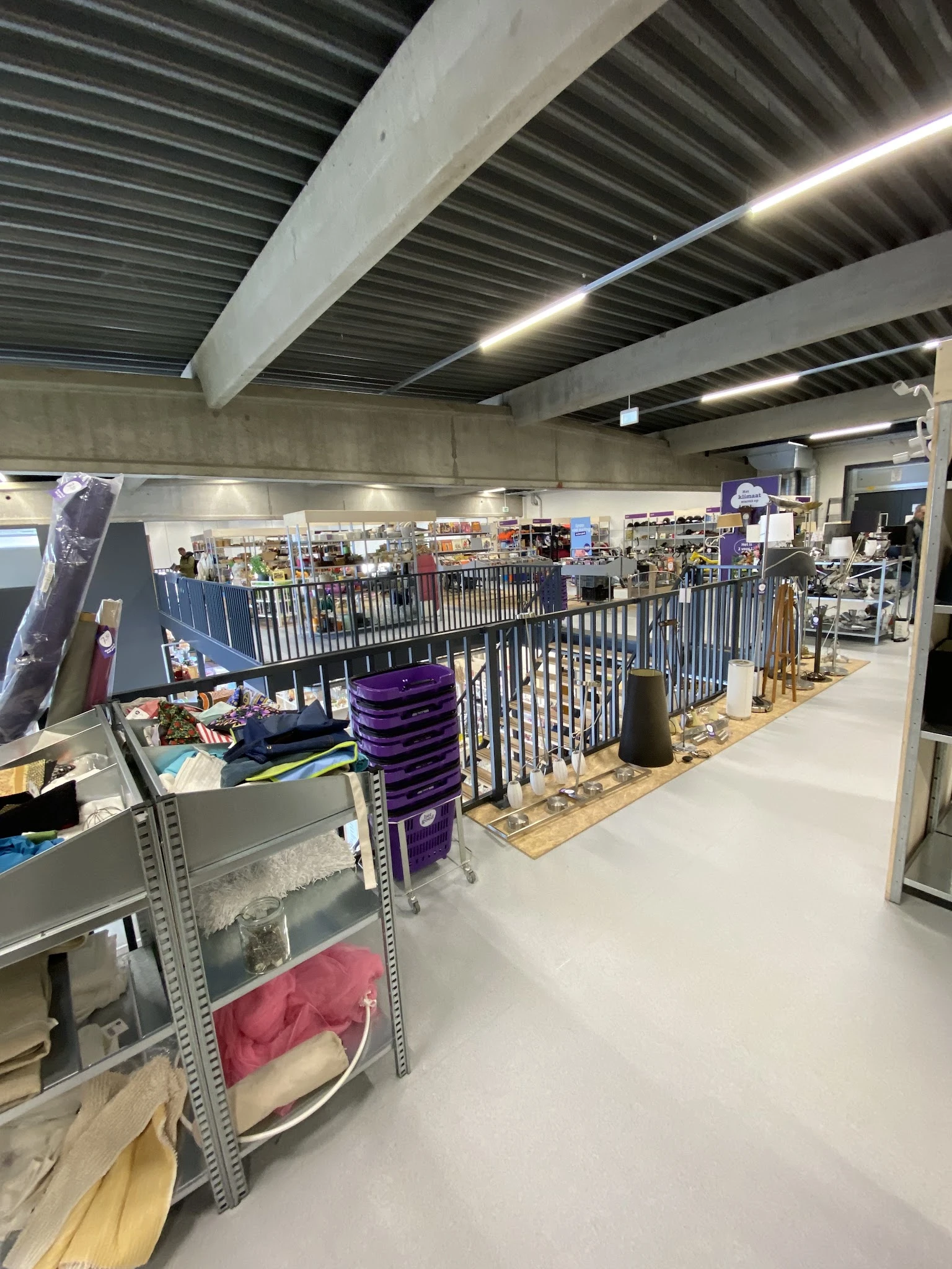 Winkelvloer met stellingen, rekken met spullen en paarse stapelboxen in een kringloopwinkel