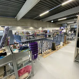 Winkelvloer met stellingen, rekken met spullen en paarse stapelboxen in een kringloopwinkel