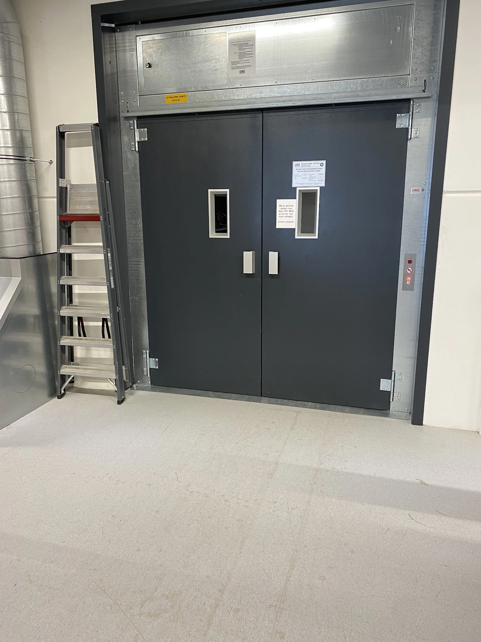 Donkergrijze dubbele deuren met witte kaders en informatiekaarten, betonnen vloer, linkszijde trap zichtbaar