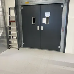 Donkergrijze dubbele deuren met witte kaders en informatiekaarten, betonnen vloer, linkszijde trap zichtbaar