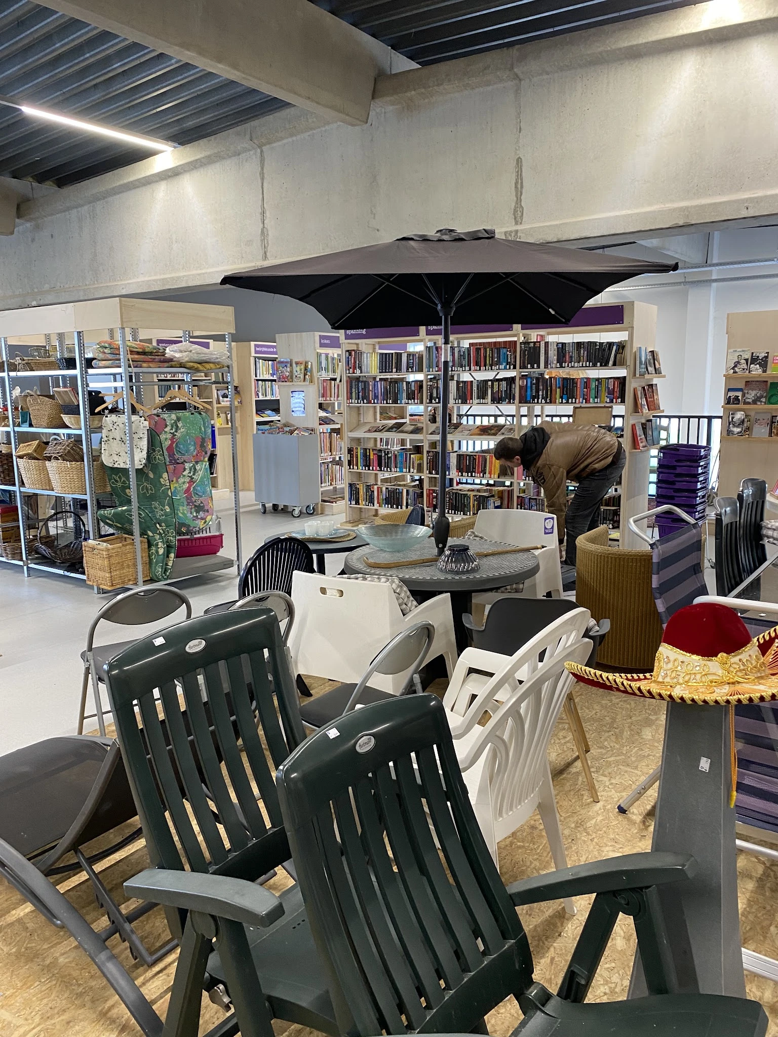 Winkelvloer met zithoeken, boekenkasten en diverse tweedehands artikelen onder zwarte parasol