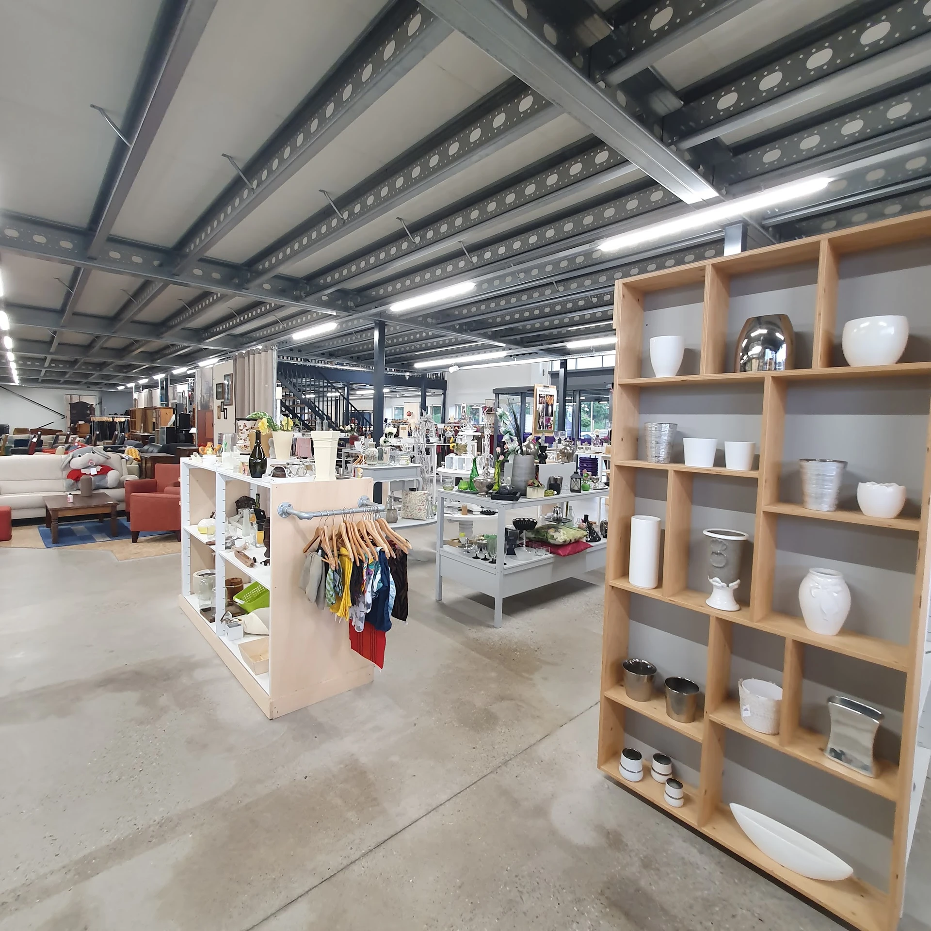 Ruim interieur van kringloopwinkel met stellingen, kledingrekken en houten kastjes met huishoudartikelen