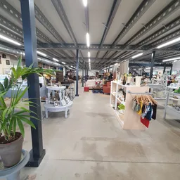 Ruim kringloopwinkelinterieur met stellingen, kledingrekken, meubels en decoratie verspreid over betonnen vloer onder industr
