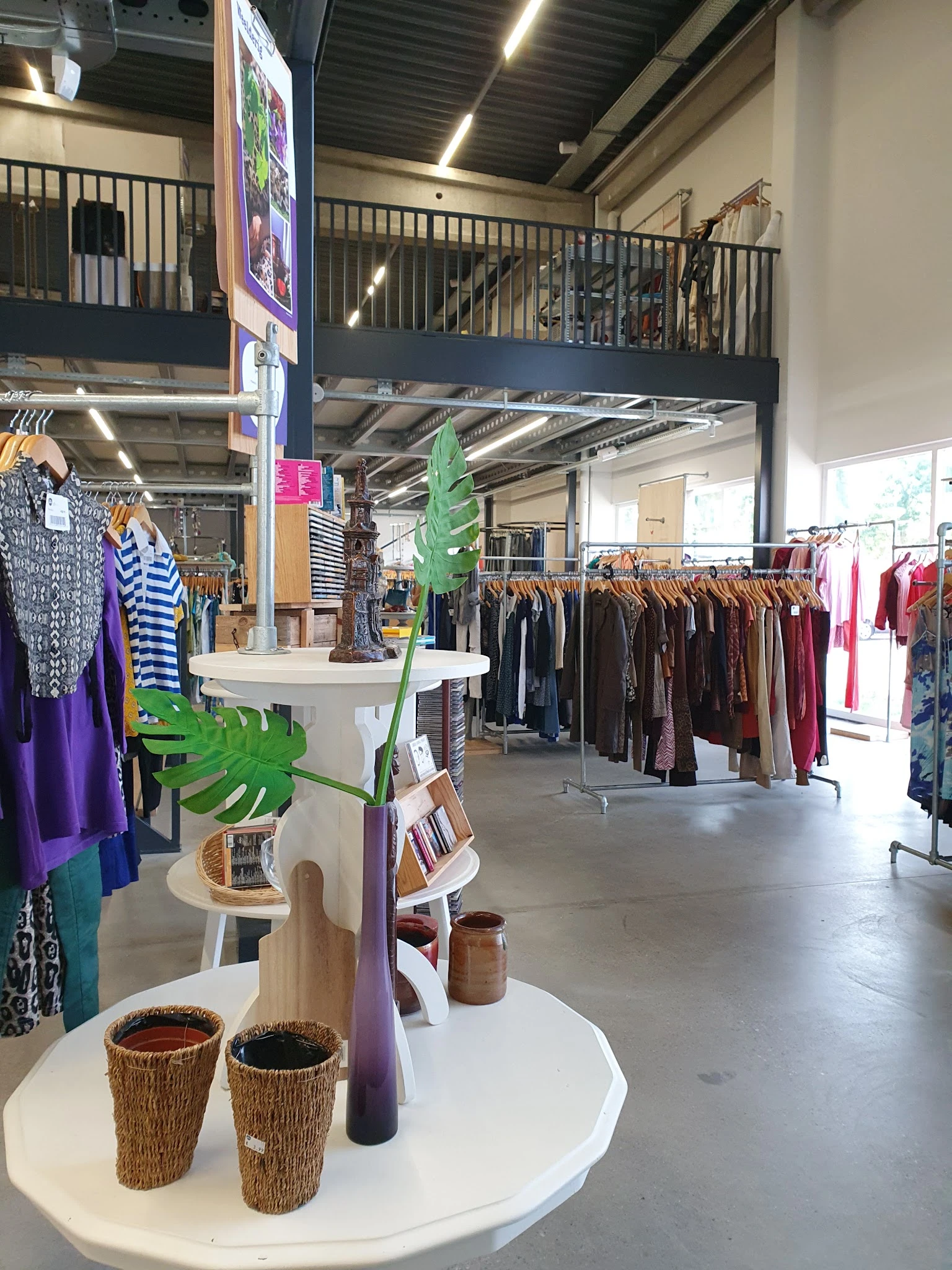 Winkelvloer met rekken vol tweedehands kleding, displaytafels en groene plantendecoratie