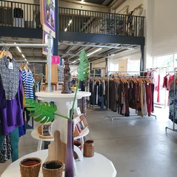 Winkelvloer met rekken vol tweedehands kleding, displaytafels en groene plantendecoratie
