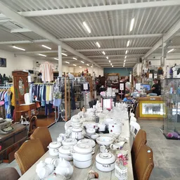 Winkelvloer van kringloopwinkel met tafels met serviesgoed, kledingrekken en verschillende meubels en spullen