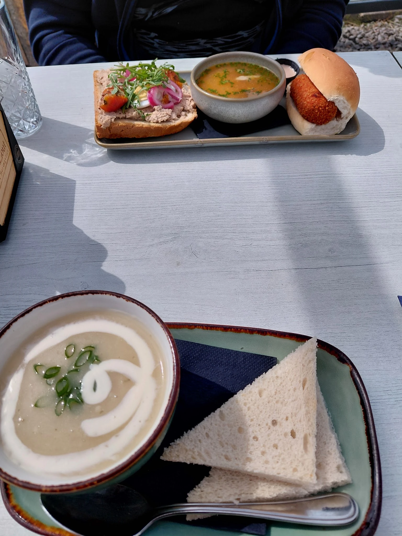 Bord met soep en wit brood op een tafel in zonlicht, met een tweede bord op achtergrond