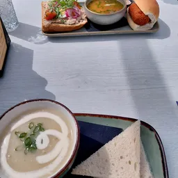 Bord met soep en wit brood op een tafel in zonlicht, met een tweede bord op achtergrond