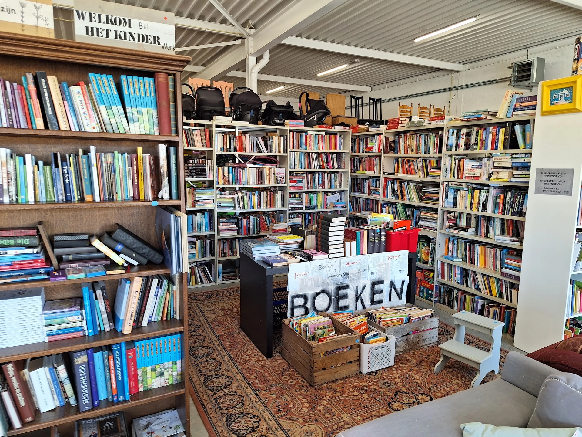 Binnenaanzicht kringloopwinkel met boekenkasten langs de wanden en centrale display met 'BOEKEN' opschrift