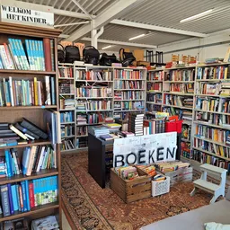 Binnenaanzicht kringloopwinkel met boekenkasten langs de wanden en centrale display met 'BOEKEN' opschrift