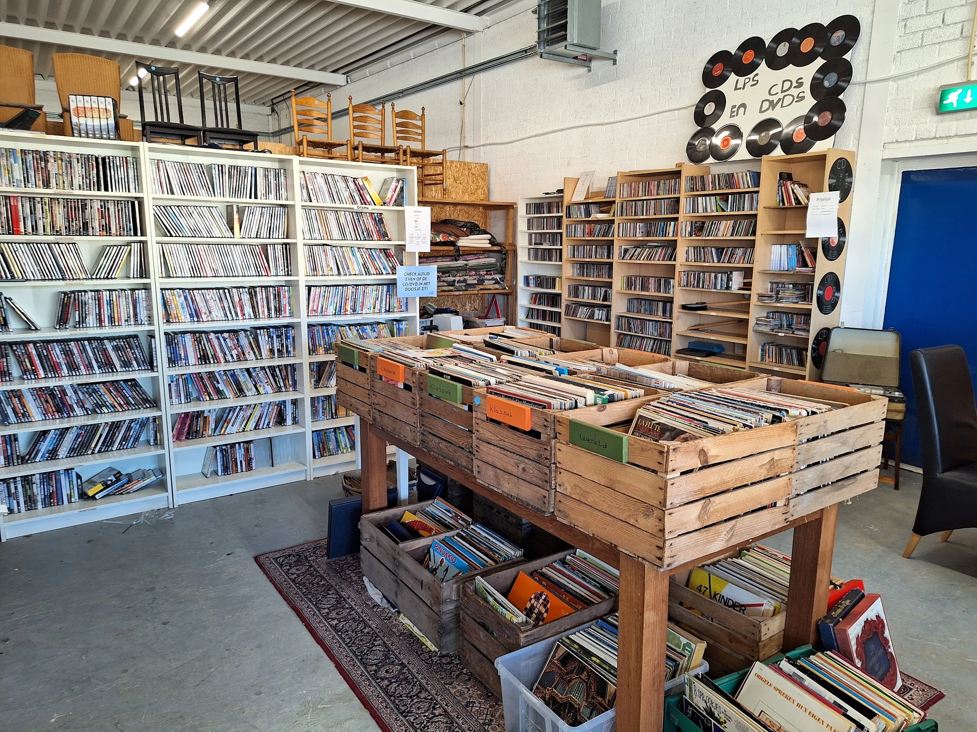 Ruime winkelruimte met cd- en platenkast, boekenkasten en houten toonbank vol met verzamelobjecten