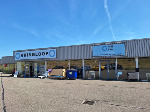 Gevel van kringloopwinkel met naam KRINGLOOP zichtbaar, enkele artikelen buiten uitgestald, heeldere dag
