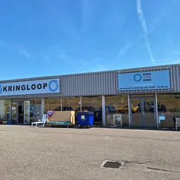 Gevel van kringloopwinkel met naam KRINGLOOP zichtbaar, enkele artikelen buiten uitgestald, heeldere dag