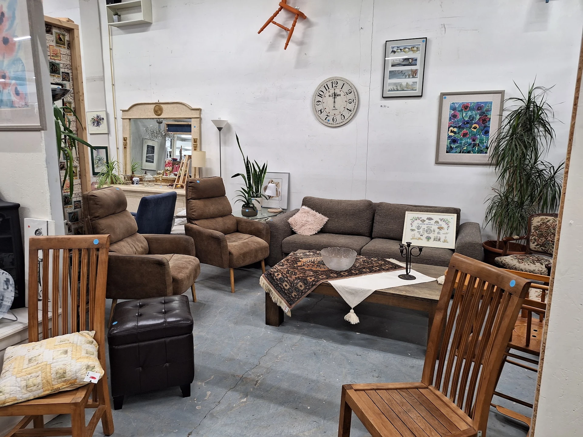 Woonkamer-inrichting in kringloopwinkel met bruine fauteuils, grijze bank, houten stoelen en diverse huisraad