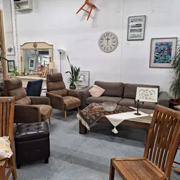 Woonkamer-inrichting in kringloopwinkel met bruine fauteuils, grijze bank, houten stoelen en diverse huisraad