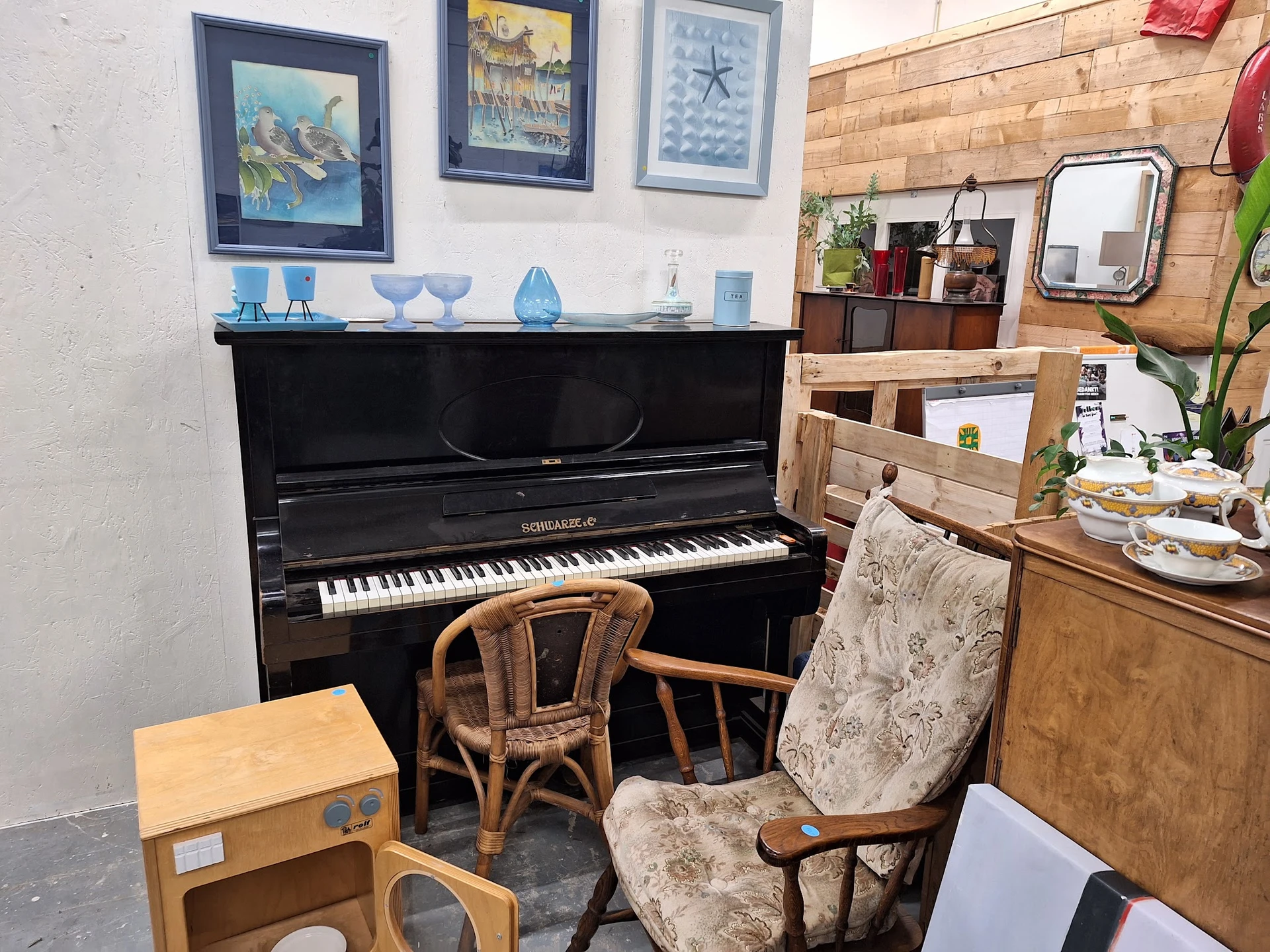 Interieur van kringloopwinkel met zwarte piano, houten stoelen, kasten en diverse meubelen en decoratie aan de muur