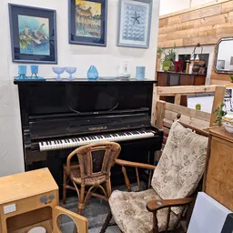 Interieur van kringloopwinkel met zwarte piano, houten stoelen, kasten en diverse meubelen en decoratie aan de muur