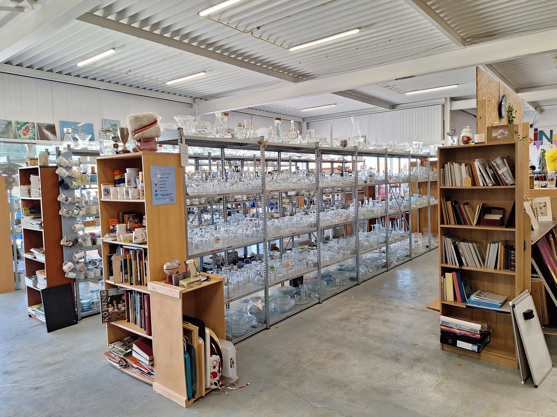 Ruime winkelhal met glazen vitrines in het midden en houten stellingen met boeken en spullen aan de zijkanten
