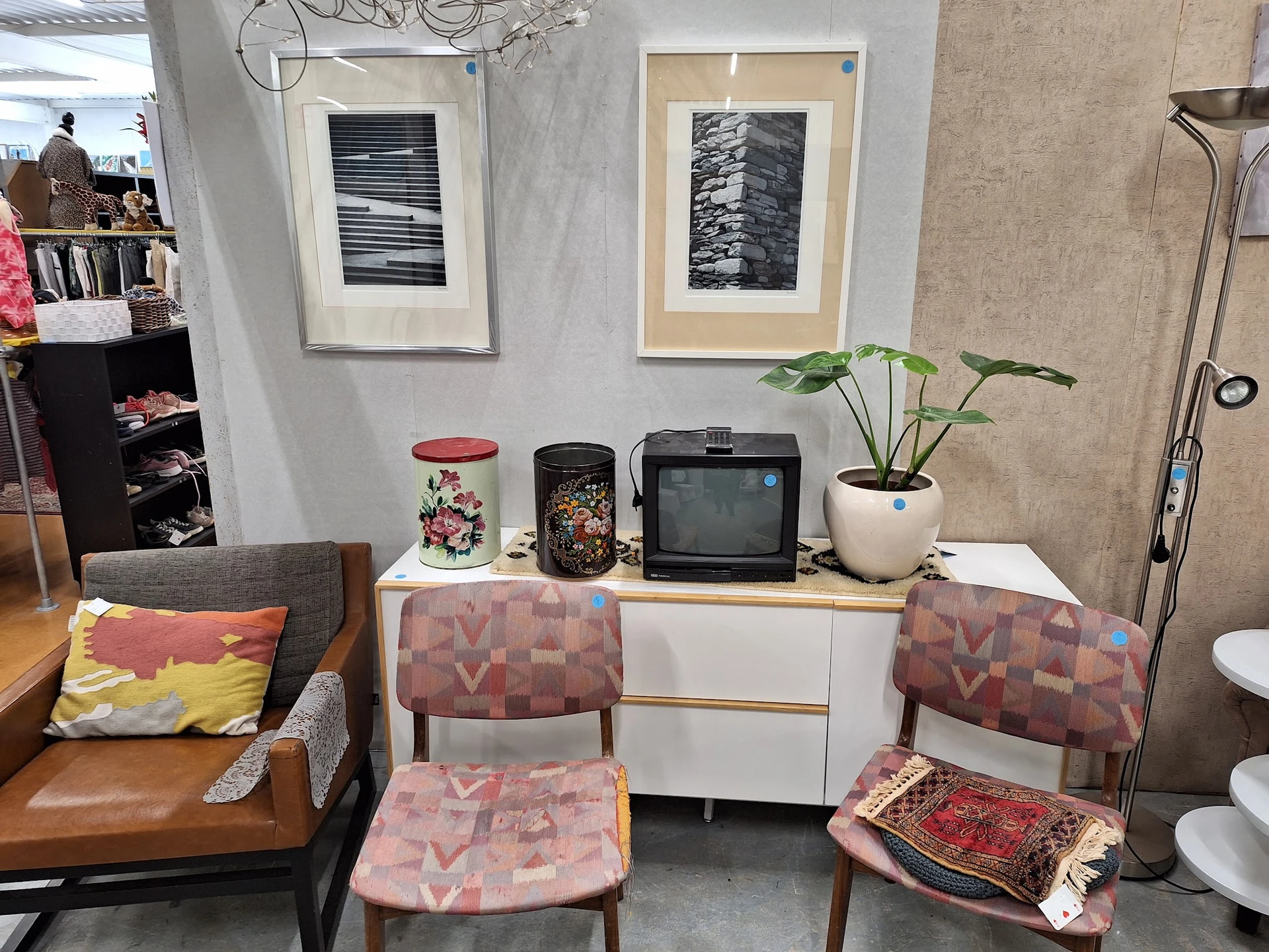 Winkelinterieur met meubels, twee framed kunstwerken aan de muur, een commode met diverse decoratieve items en planten