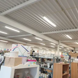 Binnenaanzicht van kringloopwinkel met stellingen, kasten en diverse gebruiksartikelen onder rioleringsdak met LED-verlichtin