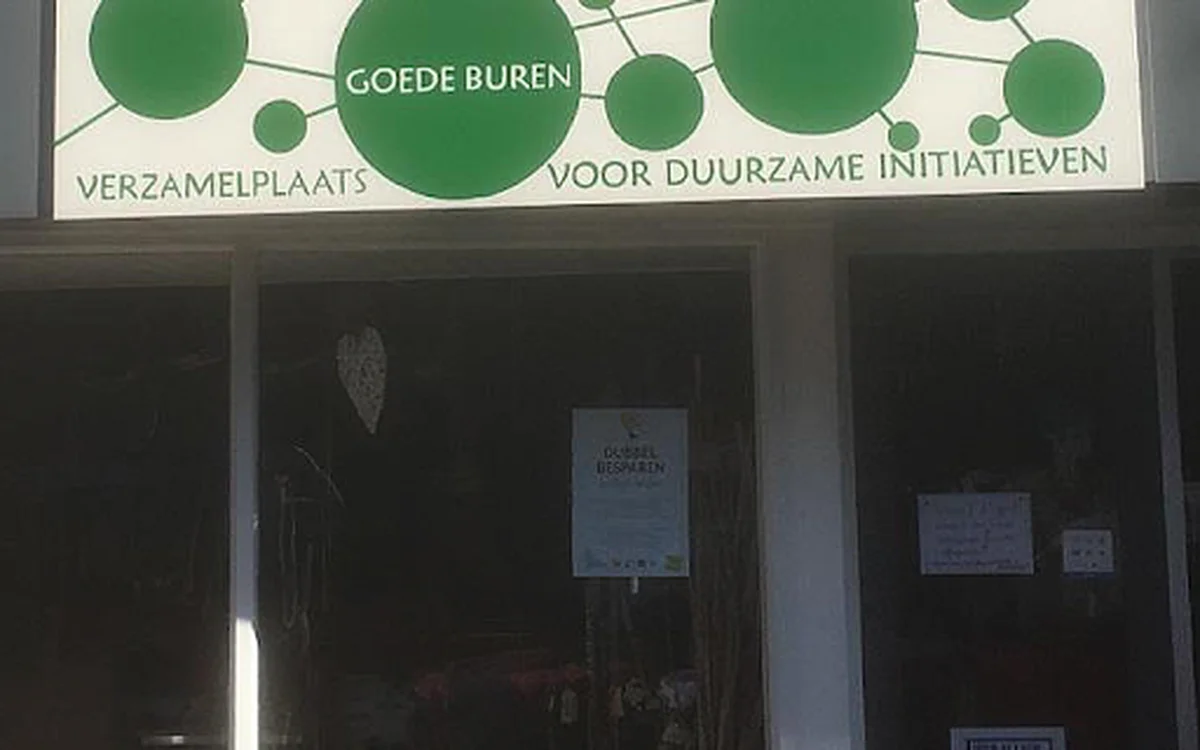 Winkelpui van Goede Buren met groene logo's en ronde cirkels op de gevel, donkere etalageruiten met enkele posters