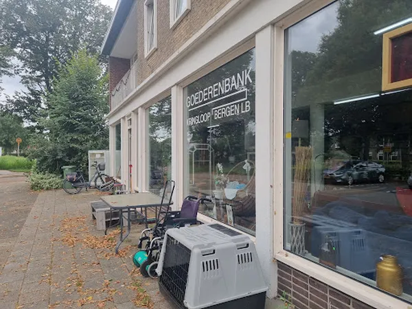 Voorgevel van kringloopwinkel met grote ramen, winkelnaam op raam, terras met stoelen en dierenbench daarvoor