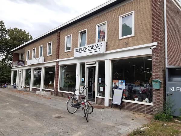 Bakstenen winkelpand met witte puien en ramen, naam Goederenbank zichtbaar, fiets ervoor, straatniveau