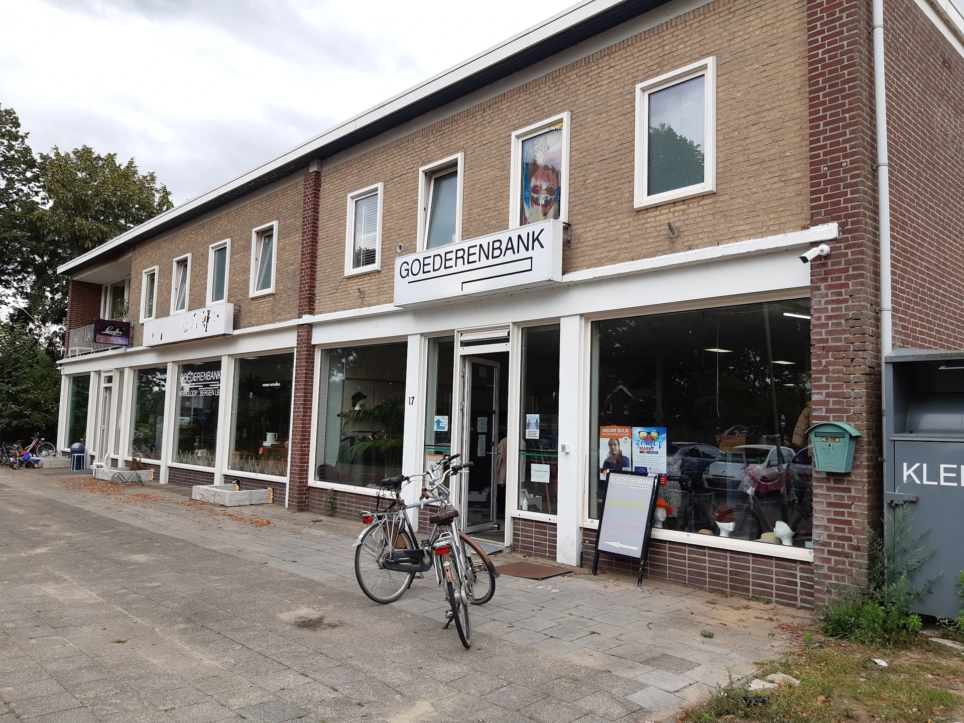 Bakstenen winkelpand met witte puien en ramen, naam Goederenbank zichtbaar, fiets ervoor, straatniveau