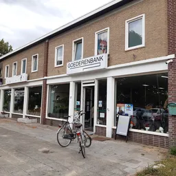 Bakstenen winkelpand met witte puien en ramen, naam Goederenbank zichtbaar, fiets ervoor, straatniveau