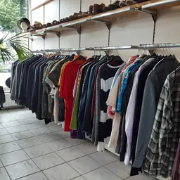 Rekken met tweedehands kleding in verschillende kleuren en stijlen, waaronder geruit patroon en rode stuks
