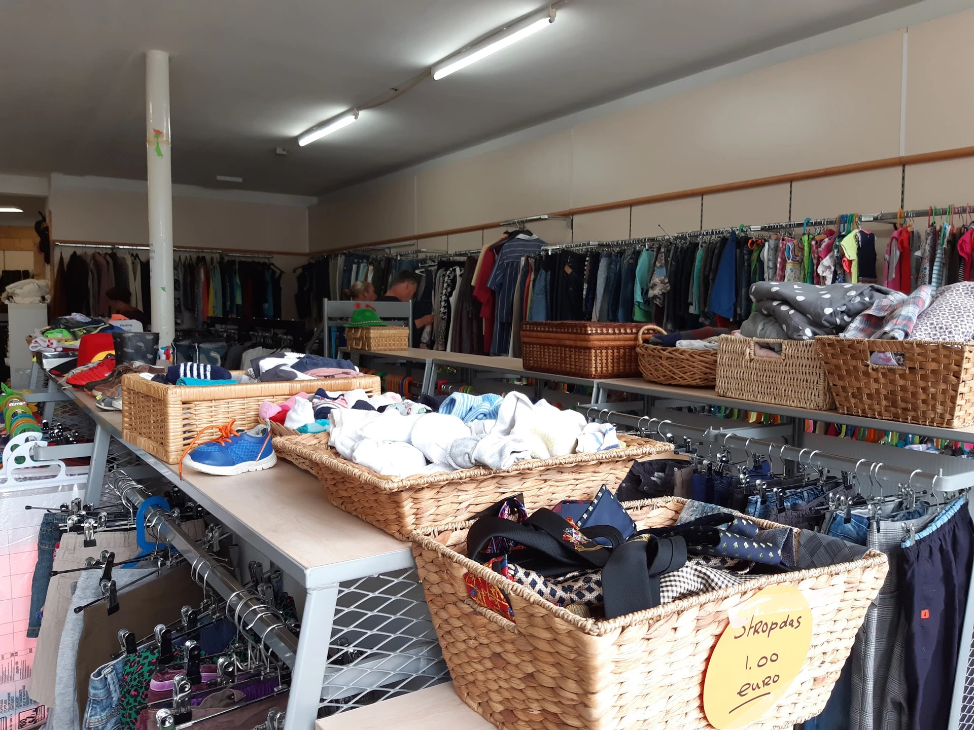Winkelvloer met rieten manden vol kleding, kledingrekken en stellingen met tweedehands kleding