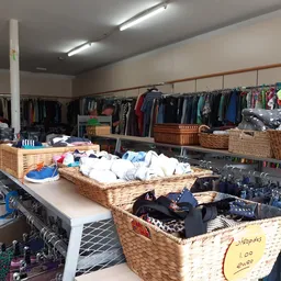 Winkelvloer met rieten manden vol kleding, kledingrekken en stellingen met tweedehands kleding