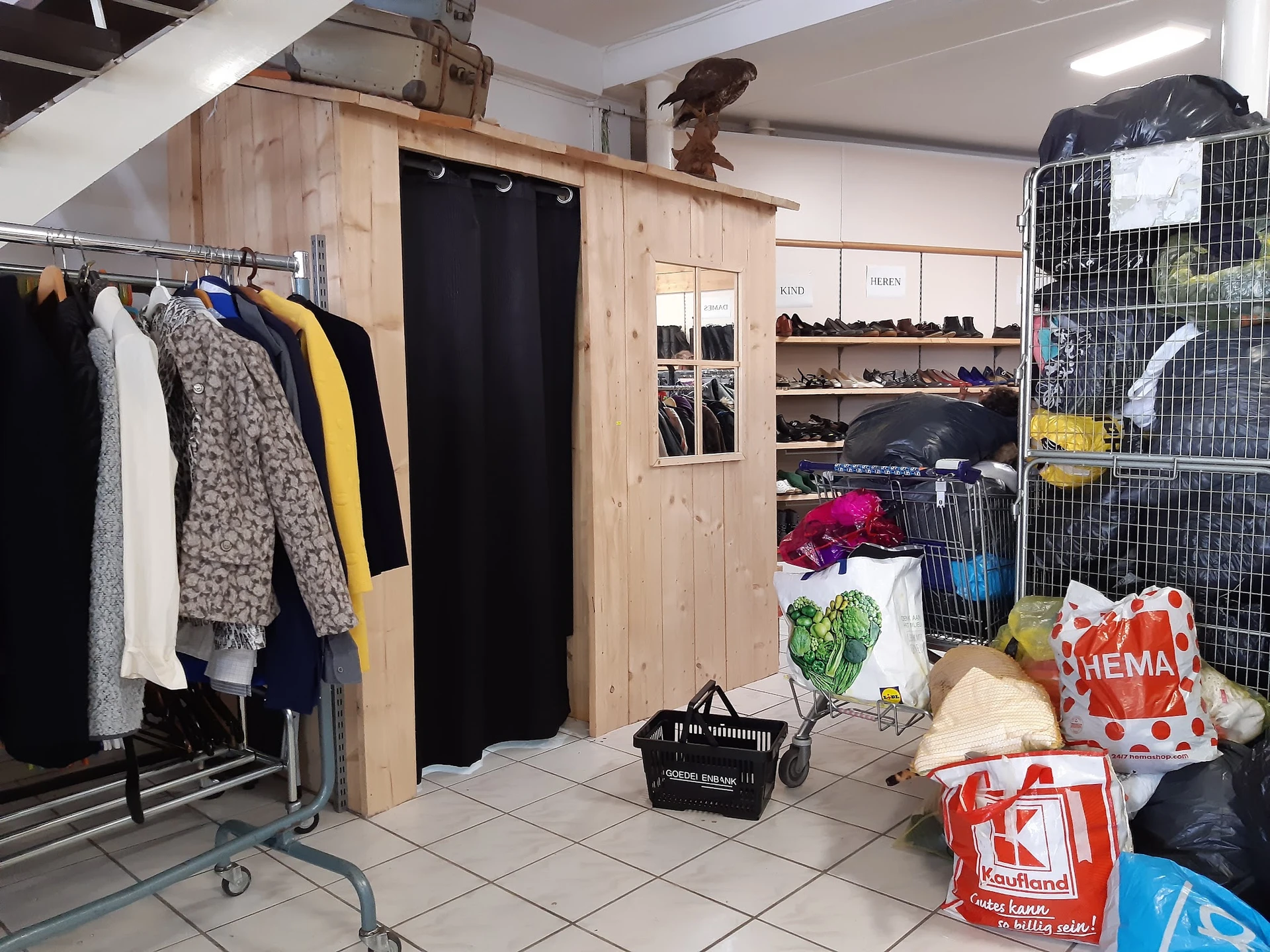 Winkelvloer met kledingrekken, houten kaststructuur met paskamer, schoenenplank en dozen met spullen
