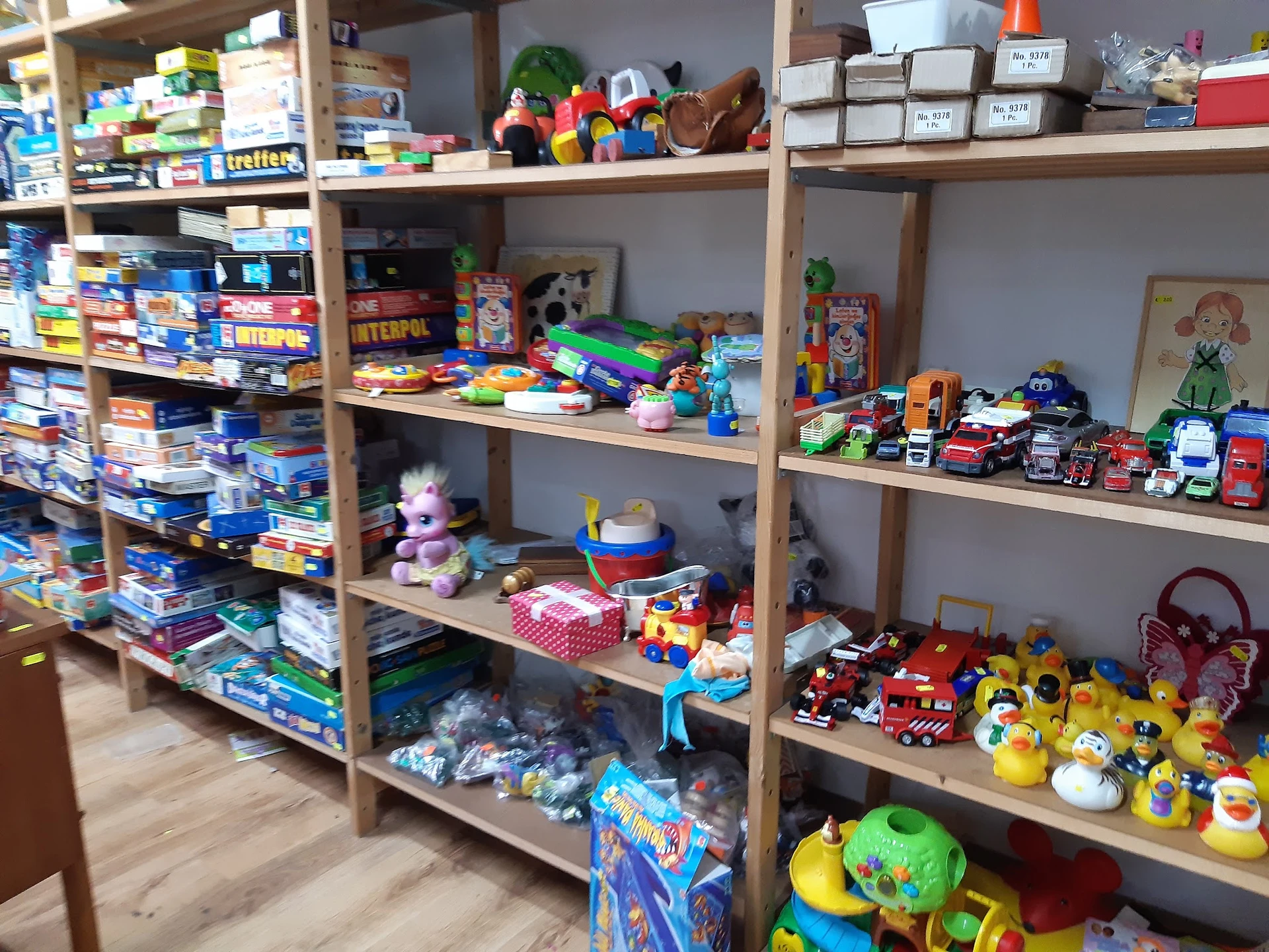 Stellingen met speelgoed, plastic speelfiguren, auto's, poppen en diverse kinderspeelgoed in de kringloopwinkel