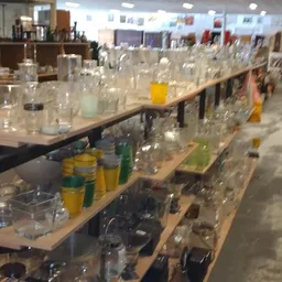 Lange werkbank met veel glazen flessen en potjes, waarschijnlijk huishoudelijke artikelen of decoratiestukken