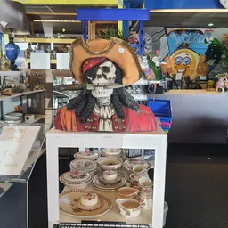 Uitgestalde decoratieve items en servies in de kringloopwinkel, inclusief een piratenskelletfiguur en aardewerk met patroon