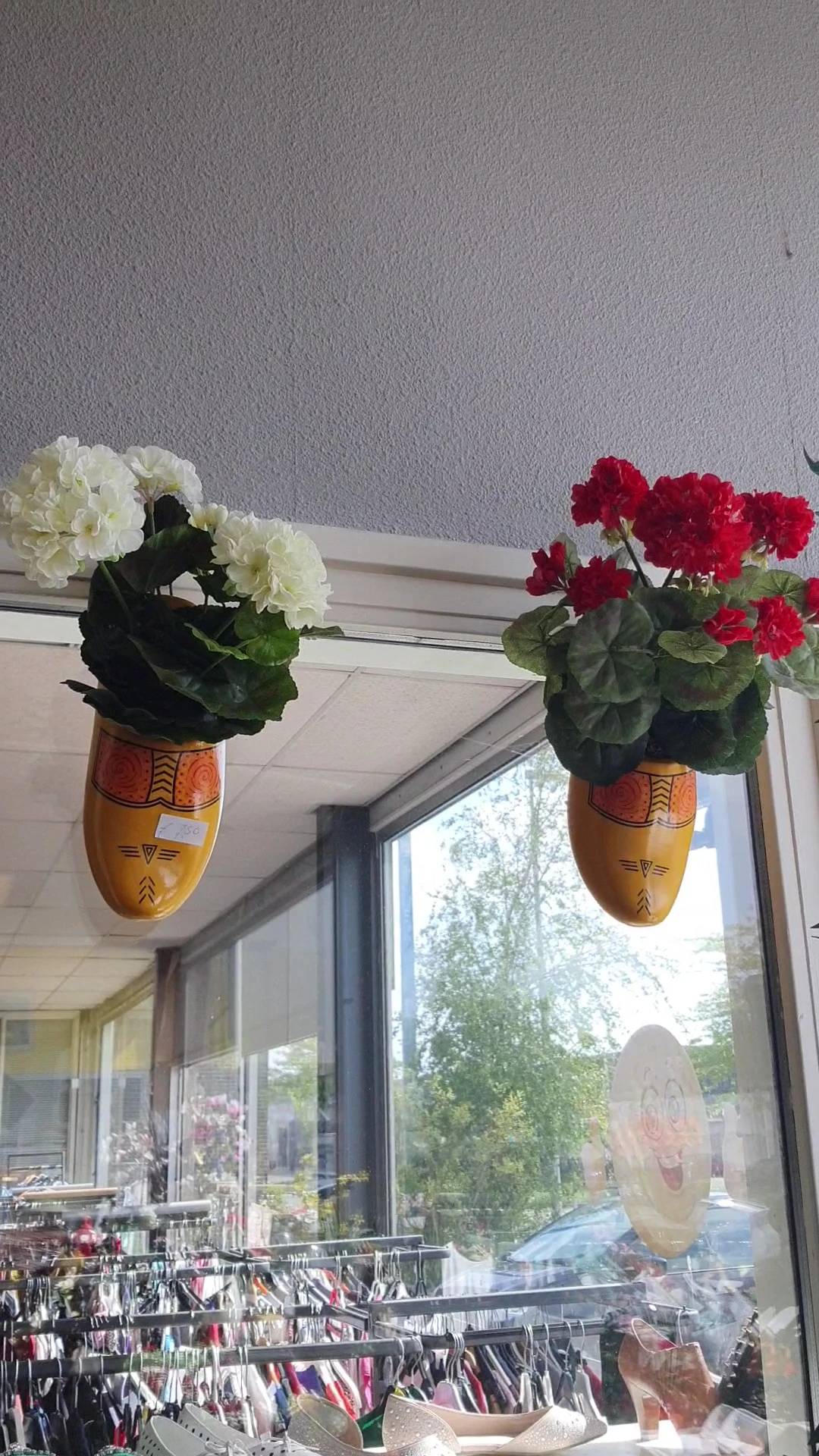 Twee gele maskervormige bloempotten met witte en rode geraniums voor een raam
