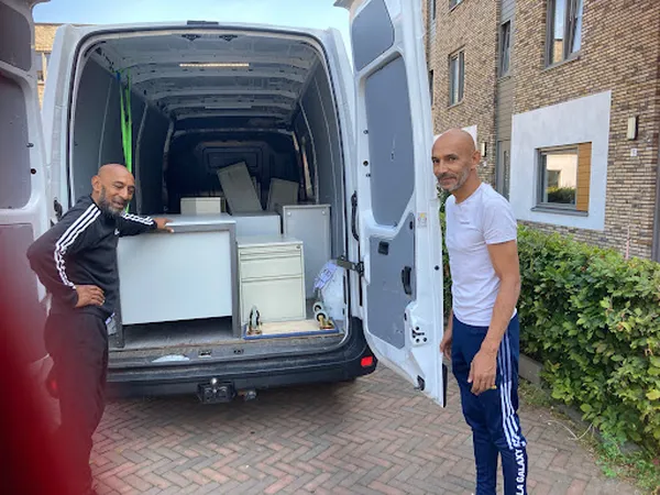 Twee mannen laden meubels in een witte bedrijfsbus op een oprit
