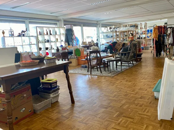 Ruim winkelbinnenland met houten vloer, kasten met spullen, meubels, kleding aan rekken en diverse tweedehands artikelen vers