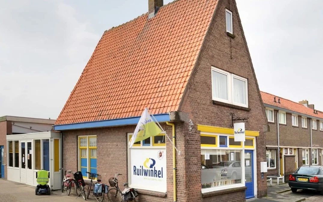 Bakstenen winkel met rode dakpannen, blauwe en gele details, en de naam 'Ruthwinkel' op de voorgevel