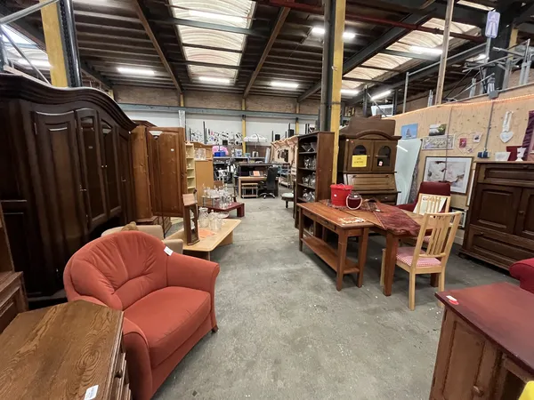 Winkelvloer met houten meubels, rode stoelen, kasten en diverse tweedehands spullen onder industrieel plafond