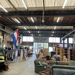 Ruim magazijnachtig interieur van kringloopwinkel met meubels, kleding en diverse spullen, Nederlandse vlaggen, goed verlicht