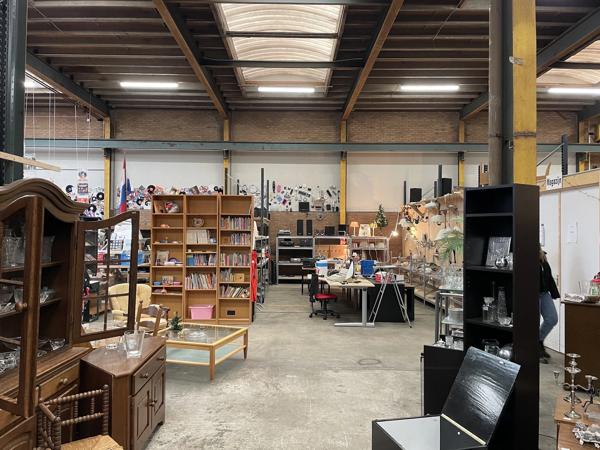 Ruim magazijnachtig interieur van kringloopwinkel met diverse meubels, boekenkasten, kasten en huishoudelijke items uitgestal