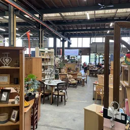 Winkelvloer met houten stellingen, meubels, decoratie en diversen in een ruime, lichte industriële ruimte