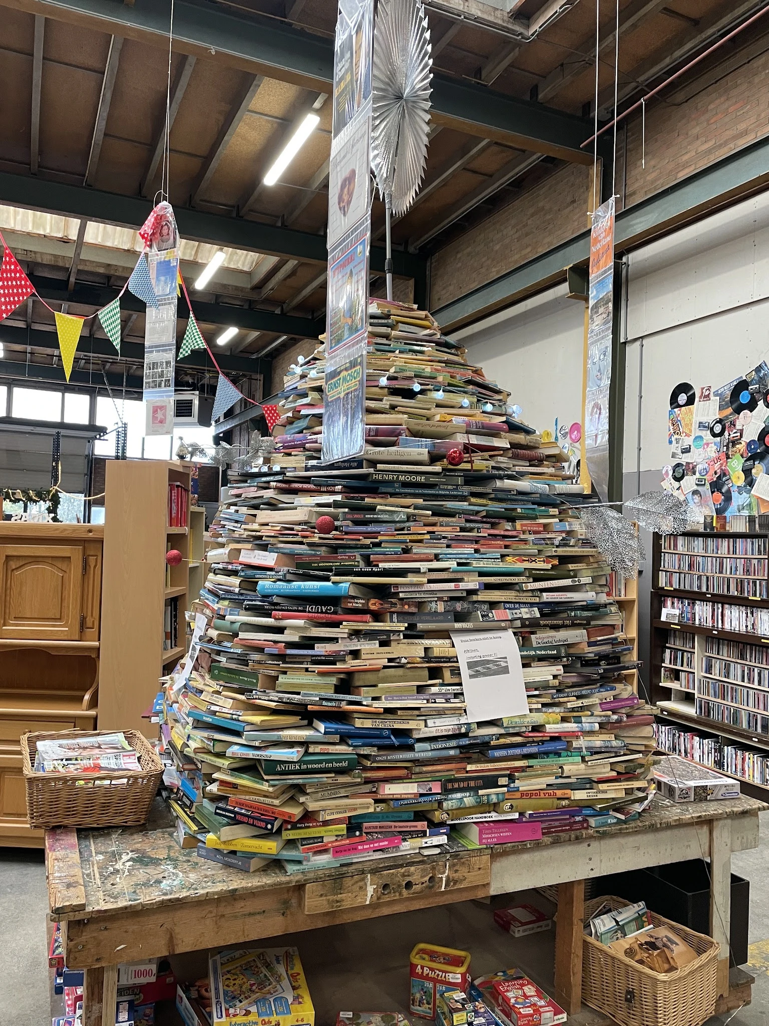 Grote piramide van gestapelde boeken in een kringloopwinkel, omgeven door boekenrekken en winkelinterieur
