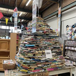 Grote piramide van gestapelde boeken in een kringloopwinkel, omgeven door boekenrekken en winkelinterieur